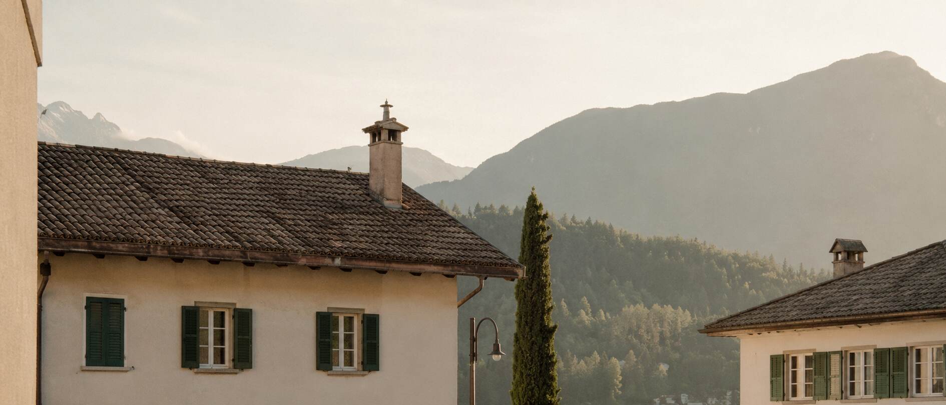 Wohnhäuser vor bewaldeter Berglandschaft im Abendlicht