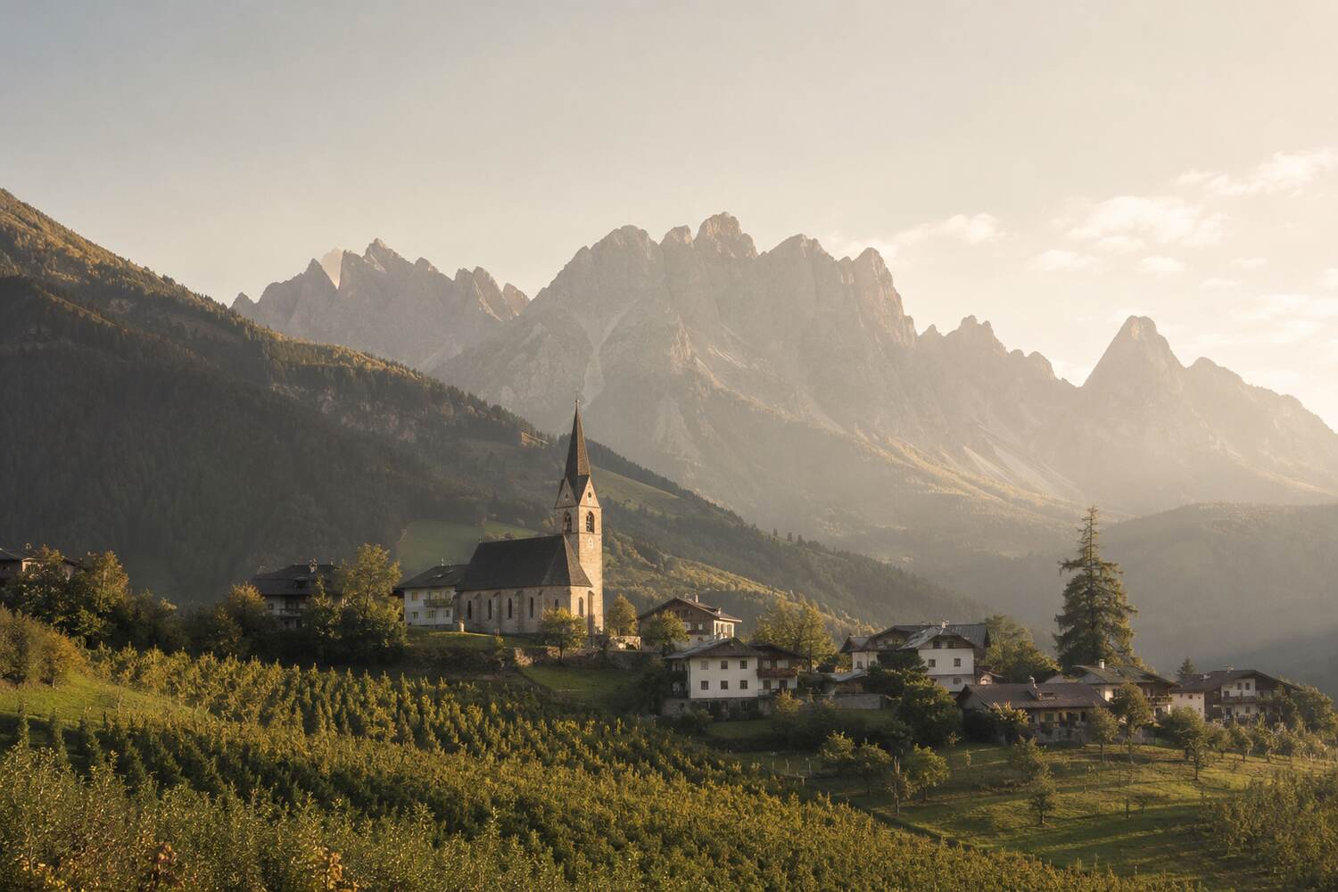 Südtiroler Dorf mit Kirche vor einer Bergkette im Abendlicht